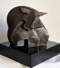A bronze sculpture of a bull with chiseled body and sharp horns; the bull bend  neck downwards adding a softness to the sharp lines,