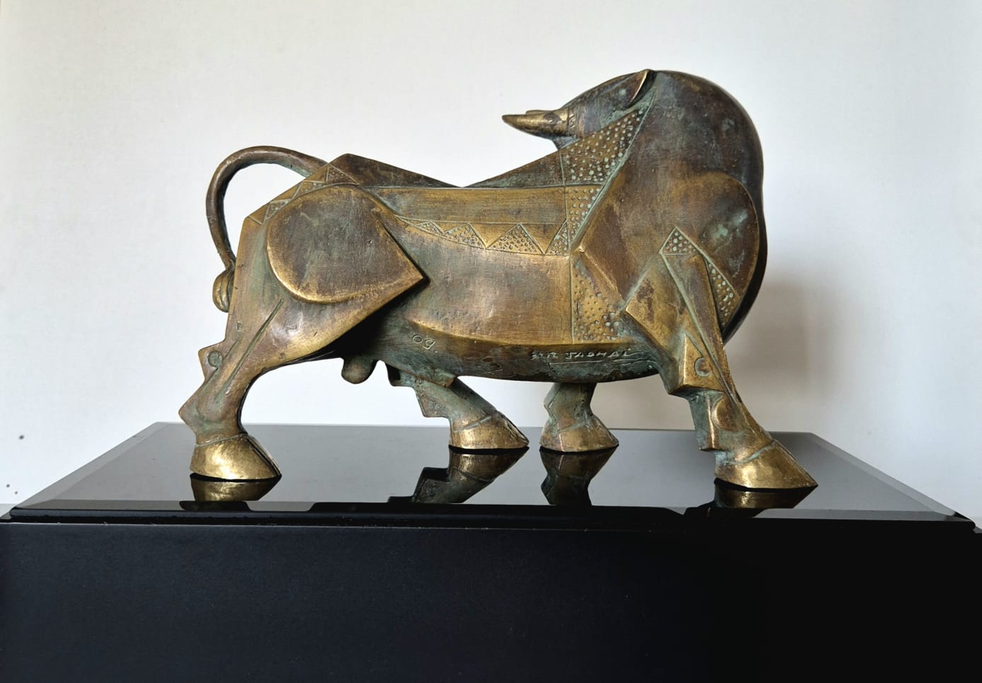 A bronze bull sculpture with geometric details, displayed on a glossy black pedestal . Backside close upImage. 