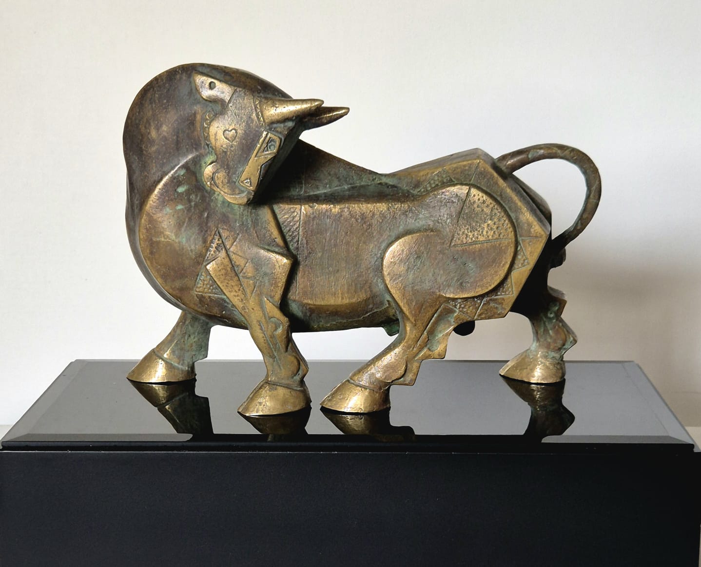 A stylized bronze bull sculpture by Dinkar Jadhav displayed on a glossy black pedestal.  