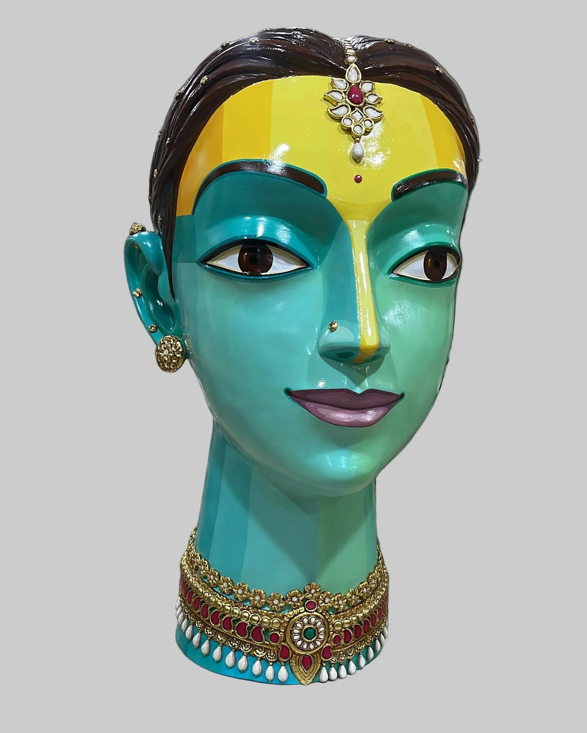 Side face Close up of Udaya Lakshmi Indian Woman Face sculpture.  The woman has yellow forehead and soft blue and green tone face as she wears jewels. 
