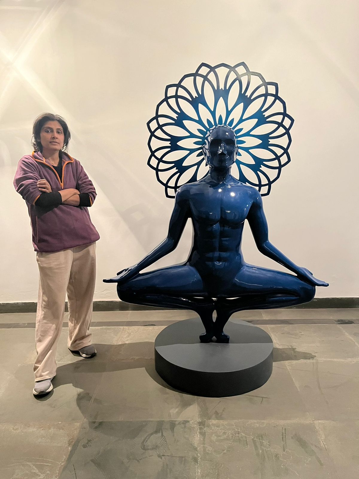 Artist Vernika Singh standing beside her 6-foot electric blue meditating man sculpture for scale reference.