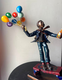 Bronze painted statue of a man skating away in work attire holding colorful balloons and a beer bottle.