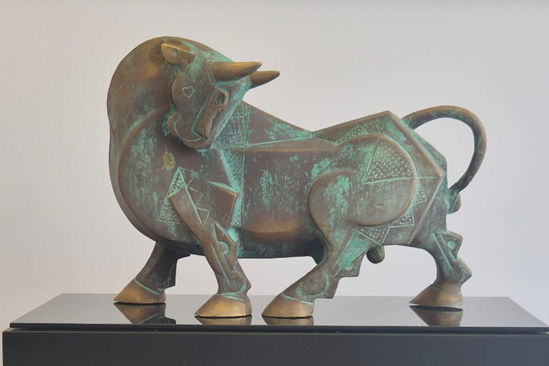 Bronze bull sculpture on a wooden pedestal with a white background